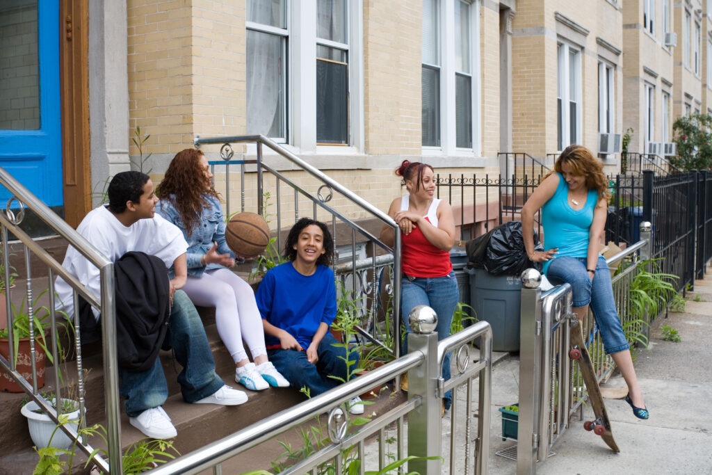Diversified group of local teens sitting on the steps of a neighborhood house.