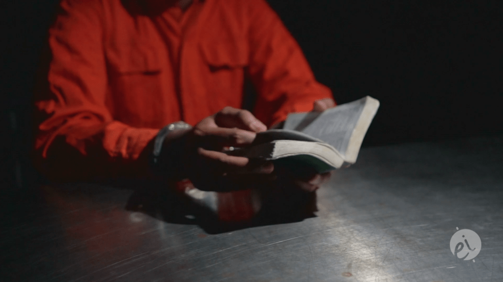 man in handcuffs and prison jumpsuit reads the bible