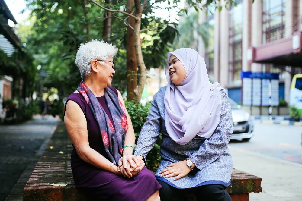 Older asian woman sits outside with middle aged muslim woman