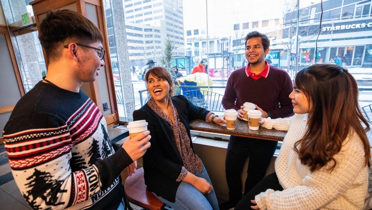 group of international students laughing in a hotel lobby drinking coffee