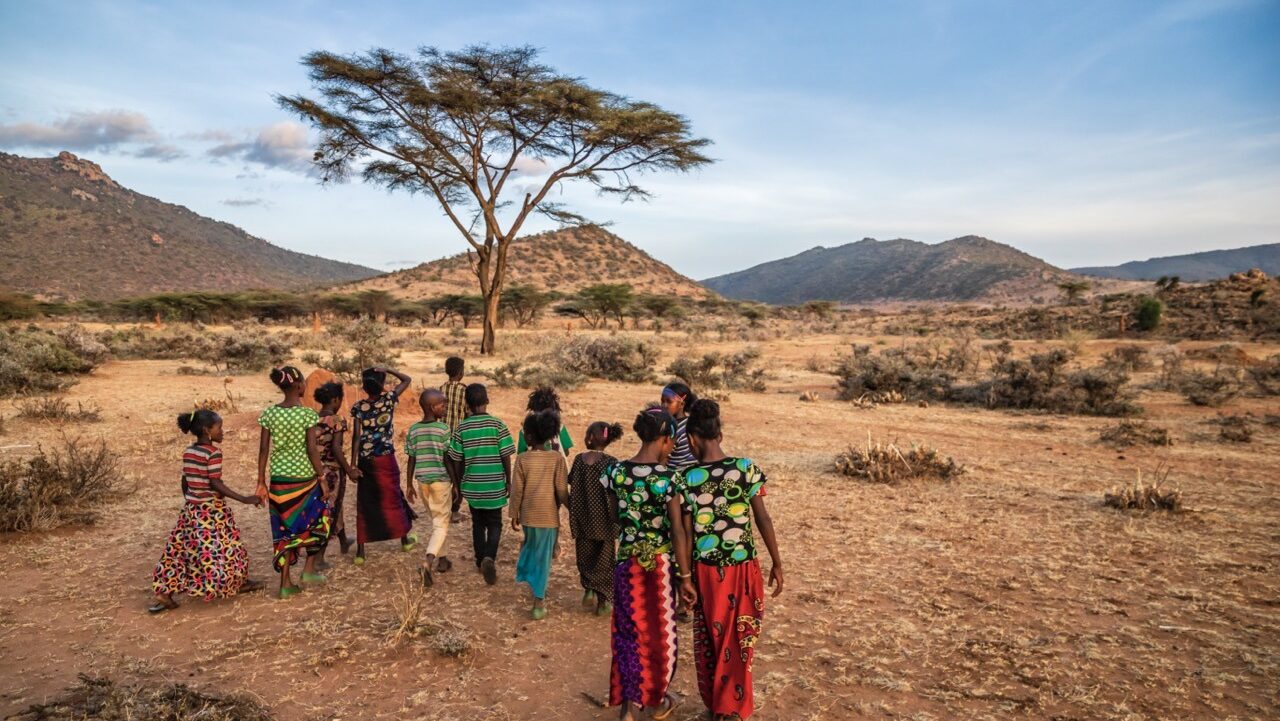 group of African children walk together across the plains holding hands