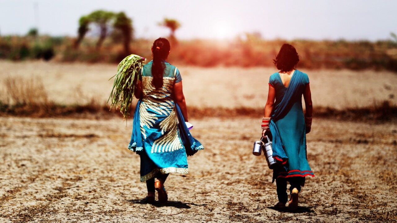 two south asian women wearing traditional clothing walk across a farm