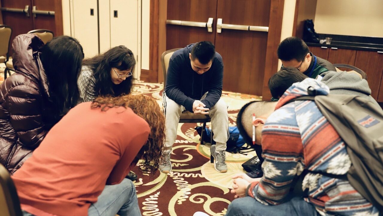 small group of international students praying together in a circle