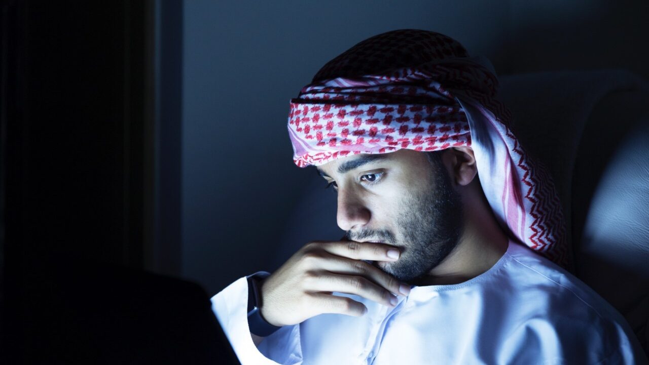 muslim man in dark room looking at a tablet