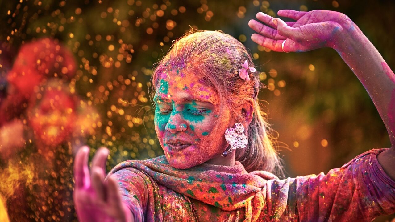 south asian woman dancing and covered in holi colored powder