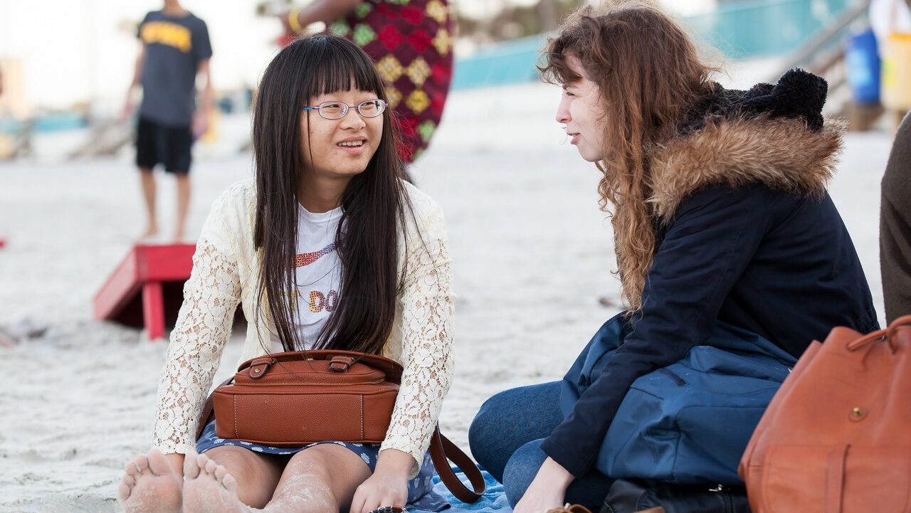 an American chats with a Chinese student while sitting on a sandy beach