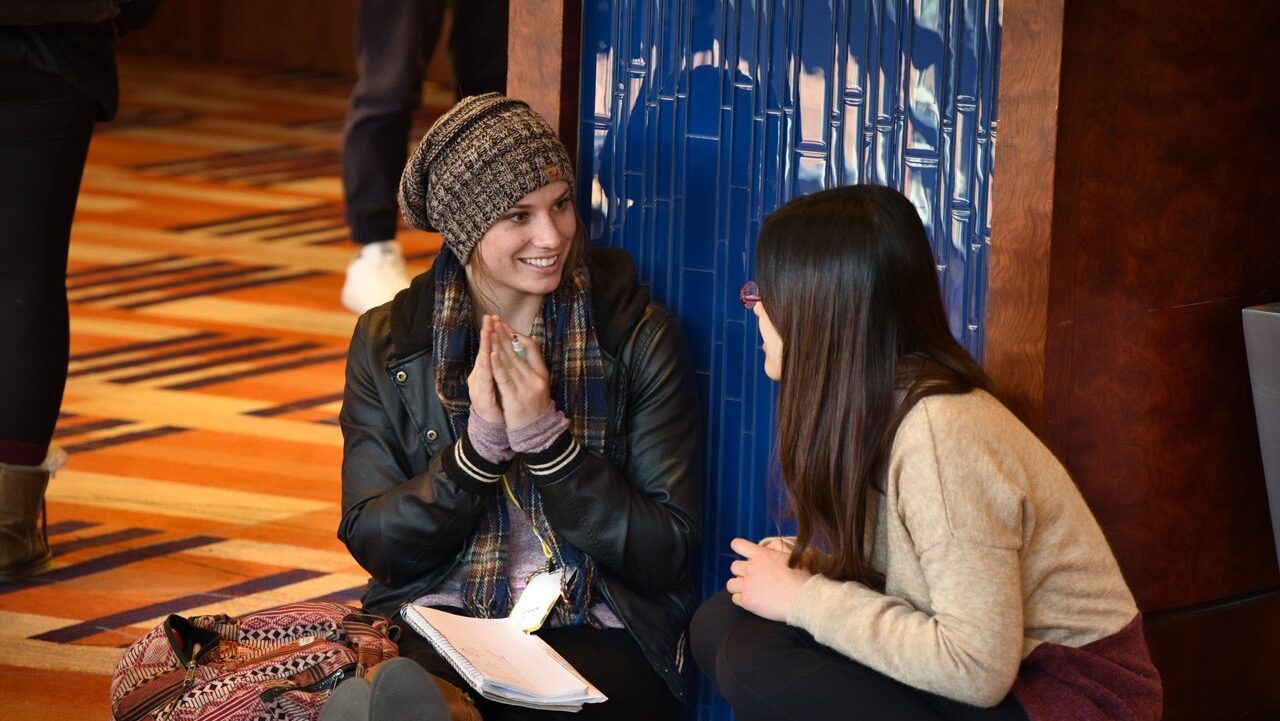 an American woman chats with a Chinese student while sitting on the floor of a hotel lobby